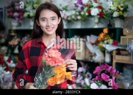 Lächelnde Frau Blumengeschäft Kleinbetrieb Blumengeschäft Eigentümer und Junger Blumenhändler untersucht Blumen im Laden Stockfoto
