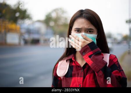 Asiatische Junge Frau, die wegen Luftverschmutzung, Partikeln und zum Schutz von Grippevirus, Influenza und Coronavirus in der Stadt mit Gesichtsmaske spaziert Stockfoto