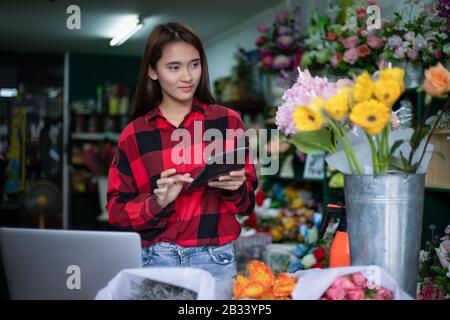 Asian Woman Florist Small Business Flower Shop Owner und Sie verwendet ihren Rechner und Laptop, um Bestellungen für ihren Laden zu übernehmen. Stockfoto