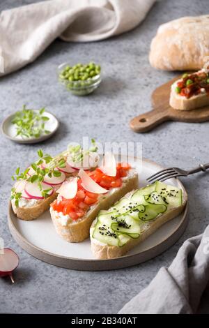 Sandwiches auf Ciabata Toast mit frischem Gemüse, Radieschen, Tomaten, Gurken und Mikrogrüns im Hintergrund. Nahaufnahme. Vertikales Format. Stockfoto