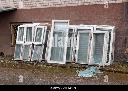Alte kaputte weiße Holzfenster werden aus dem Gebäude abgezogen, um sie durch neue Kunststofffenster zu ersetzen Stockfoto