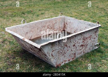 Zerknitterter rostiger Eisenbehälter zum Mischen von Flüssigputz auf einem Rasenplatz in der Nähe eines Dorfhauses Stockfoto