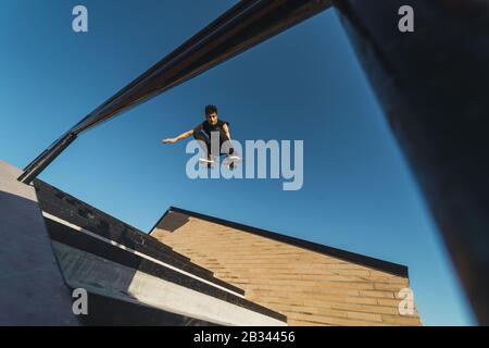 Low-Angle-Aufnahme eines kaukasischen athletischen Mannes in einem Schwarzes Outfit macht einen Flip-Trick mit einem Skateboard Stockfoto