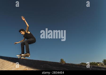 Low-Angle-Aufnahme eines kaukasischen athletischen Mannes in einem Schwarzes Outfit macht einen Flip-Trick mit einem Skateboard Stockfoto