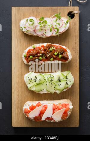 Verschiedene Sandwiches auf Toast mit frischem Gemüse, Radieschen, Tomaten, Gurken und Mikrogrüns auf schwarzem Hintergrund. Ansicht von oben. Vertikal Stockfoto