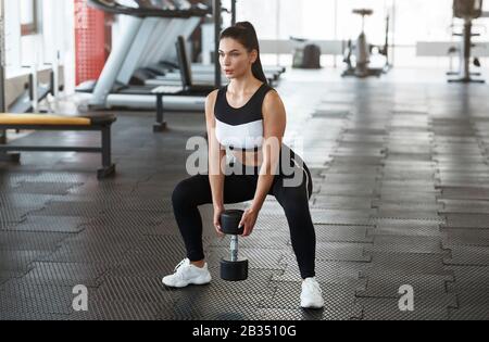 Junge Frau mit Hanteln, die im Fitnessstudio hockt Stockfoto