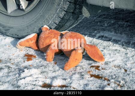 Kinderunfall auf einer Winterstraße, Hase Kaninchen Spielzeug. Tod auf der Straße, Unachtsamkeit und Gefahr. Achtung und Vorsicht. ROADKILL Winter, Blut an s. Stockfoto