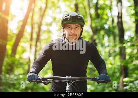 Ernsthafter Radfahrer, der in Sonnenschein auf dem Waldweg reitet Stockfoto