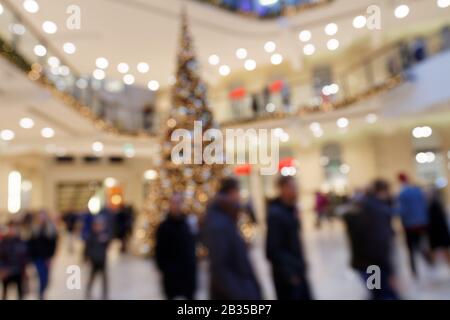 Christmas Shopping Circus: Verschwommene Szene mit dandernden Fußgängern rund um Christmas Decoration Tree in der Shopping Mall Stockfoto