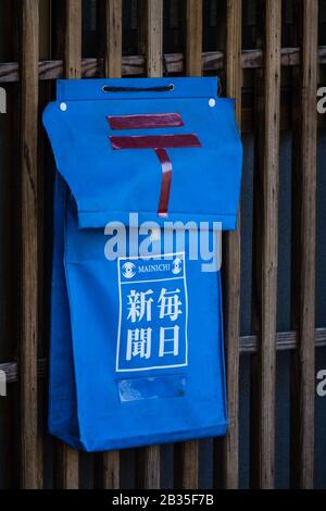 Eine Zeitung und Briefkasten auf einem Holzzaun in Nara, Japan. Das rote Symbol ist das der japanischen Post. Der Kanji liest Mainichi Shimbun. Stockfoto