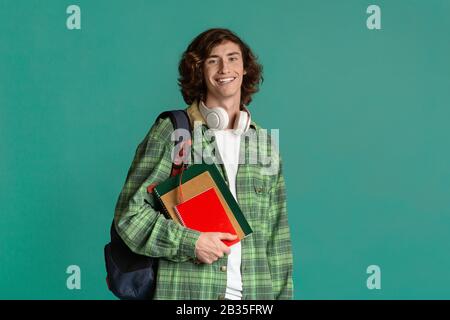 Bildungskonzept. Fröhlicher junger Mann mit Rucksack und Notizbüchern auf Farbhintergrund, Leerstand Stockfoto