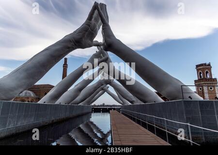 Der italienische Künstler Lorenzo Quinn baut Brücken über Venice Arsenale, Italien. Sechs Paar Hände, die eine Brücke über eine Venedig-Wasserstraße schaffen, symbolisieren die Notwendigkeit, Brücken zu bauen und Trennungen zu überwinden. Stockfoto