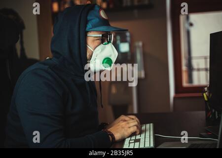 Mann, der mit Corona-Virus infiziert ist und auf dem Computer mit Atemschutzmaske im Gesicht arbeitet Stockfoto