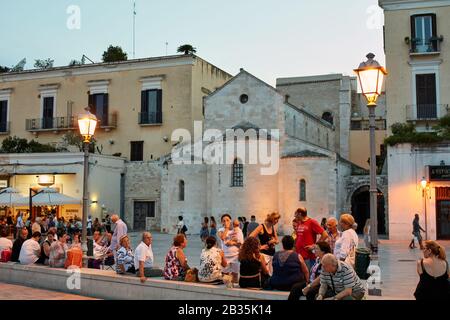 An einem Sommerabend ruhen Menschen auf der Piazza Ferrarese. Der Platz ist mit sehr belebten Bars und Restaurants gefüllt Stockfoto