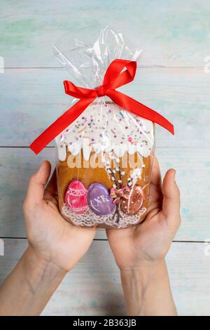 Osterdekoration. Öffnen Sie die weiblichen Hände, und halten Sie einen festlichen Lebkuchen Osterkuchen in Zellophan als Geschenk auf Holzhintergrund. Ostersympa Stockfoto