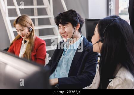 Lächelnder asiatischer Callcenter-Betreiber arbeitet gerne mit seinen Kollegen im Büro zusammen. Konzept für Business, Teamarbeit, Büro-Lifestyle. Stockfoto