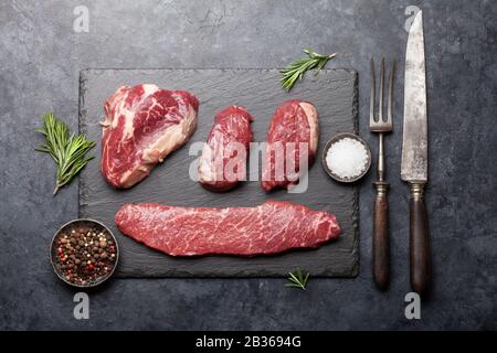 Auswahl an frischen rohen Rindersteaks mit Gewürzen auf Steinplatten. Flache Lage von oben Stockfoto