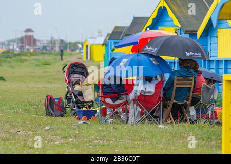 Leute, die draußen im Regen auf einem Strand sitzen, der Regenschirme hält, an einem nassen elenden regenden Bankfeiertag am Montag an einem typischen britischen Wettertag, Großbritannien. Stockfoto