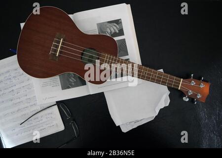 Musikalische Note, Brille und Ukulele auf schwarzem Hintergrund Stockfoto