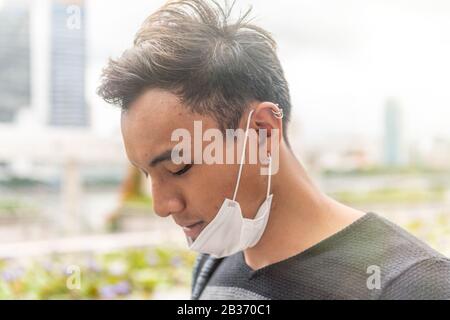 Asiatischer Mann, der im Freien Zeit mit hygienischer Maske genießt, um das Virus PM2,5 und Coronavirus zu verhindern. Luftverschmutzung, Konzept des Umweltbewusstseins. Stockfoto