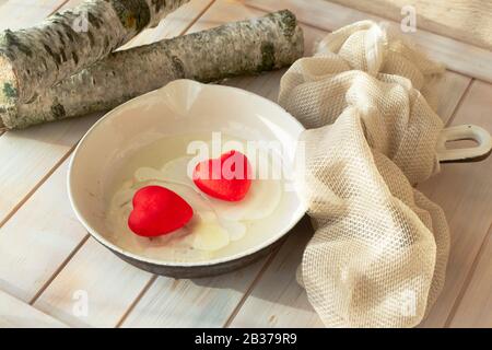 Konzeptionelles Kartenbild, Valentinstag Frühstück. Liebe lustige Speisen auf der Pfanne. Zwei rote Herzen mit Eiern. Schäbige Tabelle Stockfoto