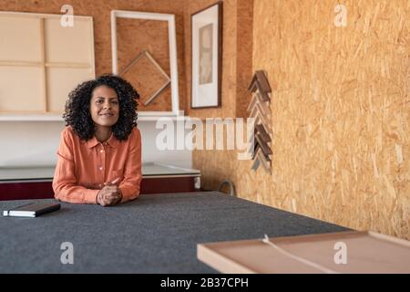 Lächelnde Frau, die in ihrem Framing-Workshop an einem Tisch sitzt Stockfoto