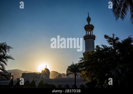 Aqaba, JORDANIEN - 31. JANUAR 2020: Sonne wirft Lichtstreuungen über die schöne weiß getünchte Moschee von Sharif Hussein bin Ali in Aqaba, Jordanien. Wolkenloser klarer Himmel Wintertag. Horizontaler Rahmen Stockfoto