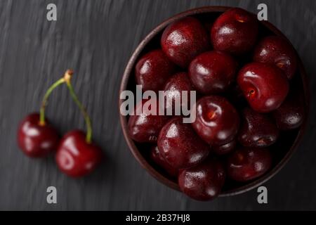 Reife und saftige Kirschbeeren auf schwarzem texturalem Hintergrund in einem braunen Kelch, mit Wassertropfen. Draufsicht, Nahaufnahme, Makro. Stockfoto