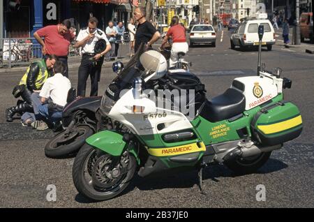London Ambulance Service Motorrad Rettungssanitäter & Polizei unterstützen Motorradkurierfahrer, die in der Straßenlage für Verkehrsunfälle in London England UK liegen Stockfoto