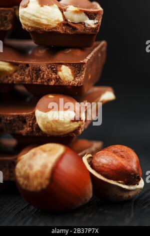 Schokolade mit Haselnüssen in Form eines Turms auf dunklem Grund, umgeben von Nüssen in der Schale und geschält. Dessertmilchschokolade mit Nüssen. Co Stockfoto
