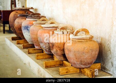 Reihe von irdenen Krüge mit Holz Deckel und rauhe graue Boden für die Wasserspeicherung in den asiatischen Haus. Selektiver Fokus auf Holz Deckel. Stockfoto