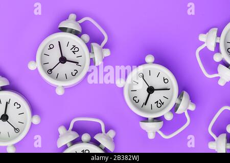 Ein Muster aus vielen klassischen weißen Weckern in Form eines Musters auf violettem Hintergrund. Draufsicht mit einer Kopie des Raumes, flacher Lay. Konzept von Stockfoto