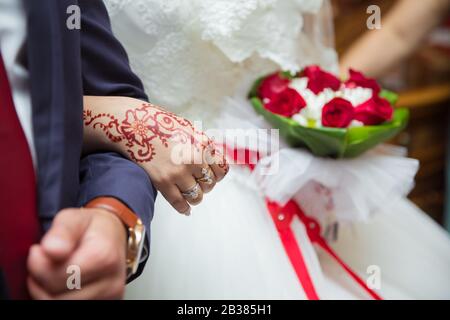 Kommen wir in die Arme des Bräutigam. Die Frau hält einen roten Blumenstrauß in der Hand. Hände und Finger werden auf Henna gezogen. Stockfoto