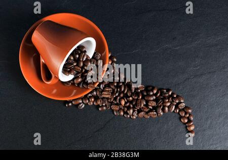 Kaffeebohnen, die aus einer Tasse und einer Untertasse verschüttet werden Stockfoto