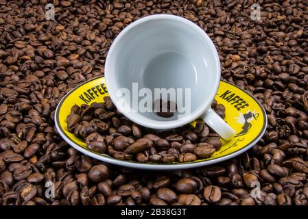 Kaffeebohnen, die aus einer Tasse und einer Untertasse verschüttet werden Stockfoto