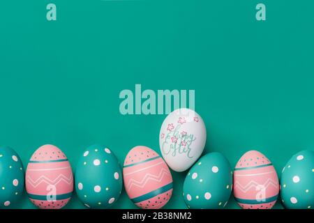 Farbige verzierte Eier auf dem neominzfarbenen Hintergrund und mit Schild Happy Easter. Osterkonzept, Karte mit freiem Kopierraum Stockfoto