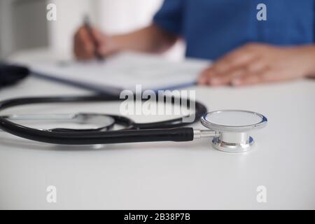 Arbeitstisch des Arztes. Stethoskop im Fokus. Doktor der weiblichen Medizin, der im Hintergrund operiert. Healthcare und Medical Concept Copy-Space. Stockfoto