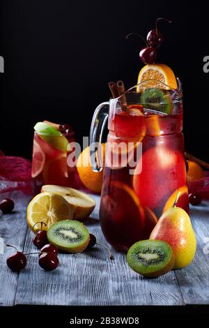 Sangria trinken in einem Glas und Dekanter mit Eis und Obst auf dunklem Hintergrund Stockfoto