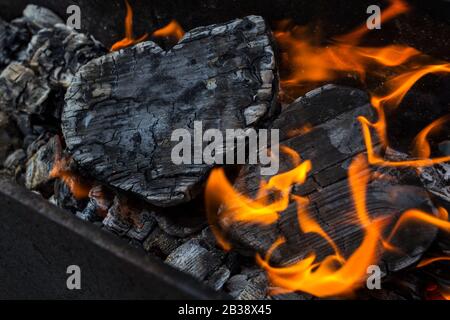 Heiße Kohlen und brennende Hölzer in Form des menschlichen Herzens. Glühende und flammende Holzkohle, leuchtend rotes Feuer und Asche. .Close-up, Draufsicht. Stockfoto