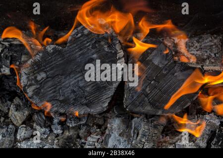 Heiße Kohlen und brennende Hölzer in Form des menschlichen Herzens. Glühende und flammende Holzkohle, leuchtend rotes Feuer und Asche. .Close-up, Draufsicht. Stockfoto