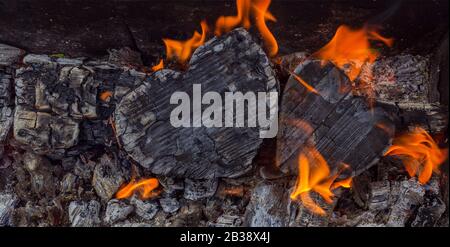 Heiße Kohlen und brennende Hölzer in Form des menschlichen Herzens. Glühende und flammende Holzkohle, leuchtend rotes Feuer und Asche. .Close-up, Draufsicht. Stockfoto