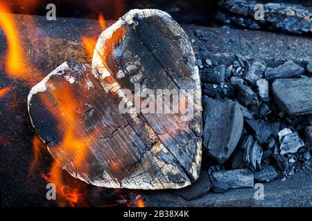 Heiße Kohlen und brennende Hölzer in Form des menschlichen Herzens. Glühende und flammende Holzkohle, leuchtend rotes Feuer und Asche. .Close-up, Draufsicht. Stockfoto