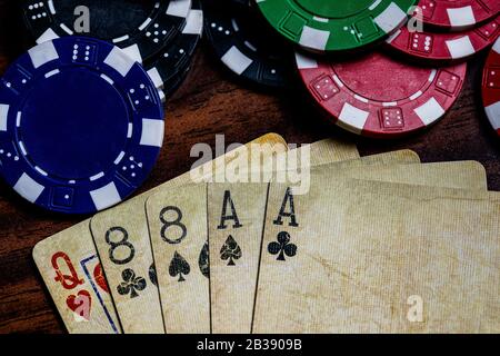 Dead Mans Hand Top Makro mit gebrauchten Karten und Pokerchips in blau, rot, grün und schwarz auf einem Holztisch mit weicher, warmer Farbtonierung. Platz für Stockfoto