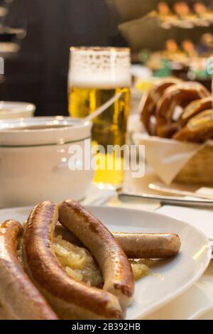 Klassisches deutsches Abendessen mit gebratenen Würstchen mit geschmortem Kohl auf großen weißen Tellern mit hellem Bier, auf dem Tisch im Restaurant. Stockfoto