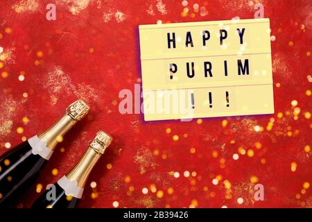 Happy Purim in Leuchtkasten und zwei Champagnerflaschen auf hellrotem Hintergrund. Purim Celebration Konzept. Kopierbereich, Draufsicht Stockfoto