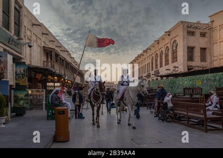 Souk Waqif Doha, Tageslichtansicht auf der Hauptstraße von Katar mit traditionellen Reitpferden der Polizei und Qatari-Flagge im Hintergrund Stockfoto