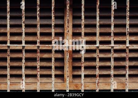 Rostiger alter Holzlüftungs-Kühlergrill mit Eisenstangen-Schutz auf alter Lagerhausbetonwand, Hualien, Taiwan. Minimalistisch, einfach Stockfoto