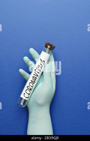 Hand in Schutzhandschuh hält Laborröhre mit abstraktem Coronavirus auf blauem Grund. Chinesisches wuhan Coronavirus 2019-nCoV-Virenschutzkonzept, flacher Lay, Kopierraum Stockfoto