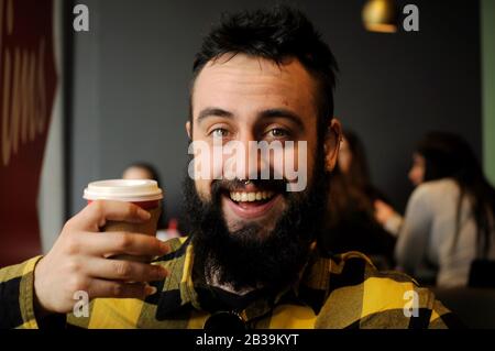 Junger Mann, der früh am Morgen in einem Café Kaffee trinkt/ein großes Lächeln hat Stockfoto