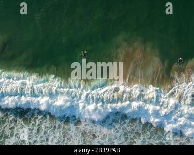 Drone Blick auf schöne türkisblauen Wellen brechen auf sandigen Küste. Luftaufnahme von goldenem Strand, tiefblauem Meerwasser und schäumenden Wellen Stockfoto